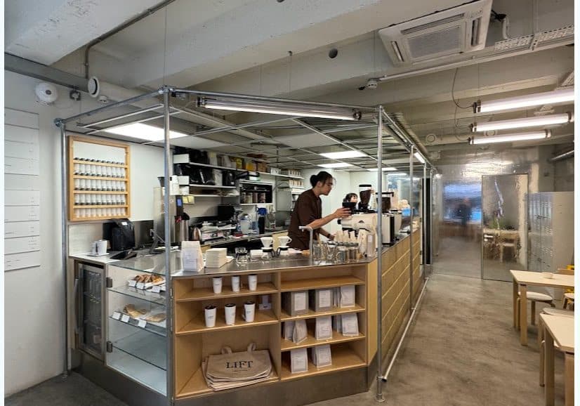 Inside LIFT Coffee: a barista at the counter with wooden shelving, and small wooden tables beyond.