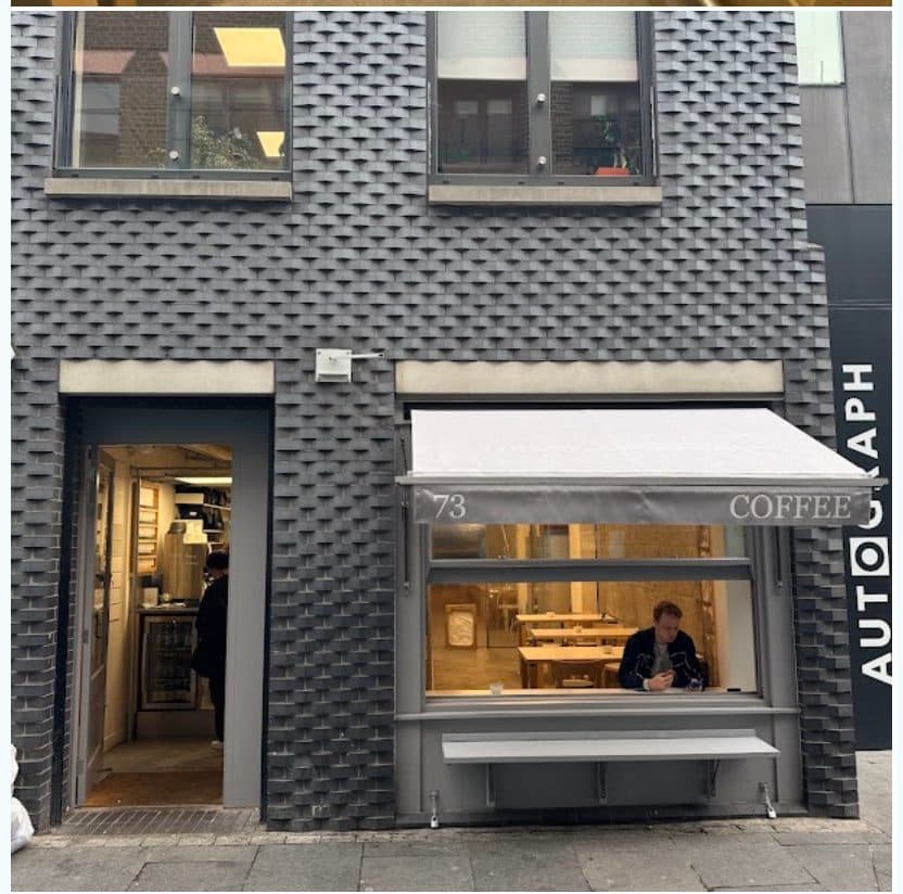LIFT Coffee shopfront on Rivington Street: dark charcoal brick, an open door and a window under a grey awning marked 73 Coffee.